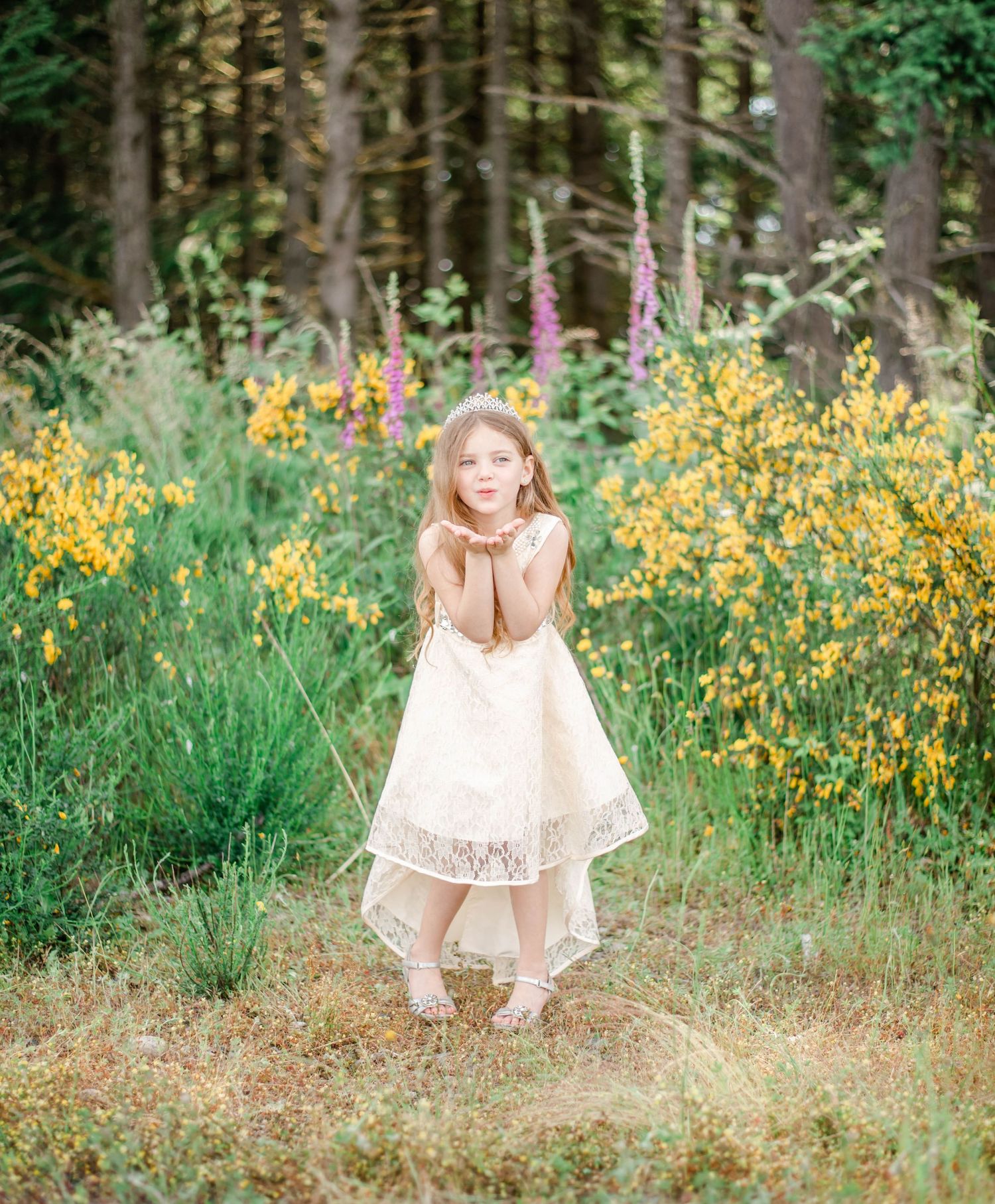 Someone in a light dress twirls playfully among vibrant yellow wildflowers near a wooded area.