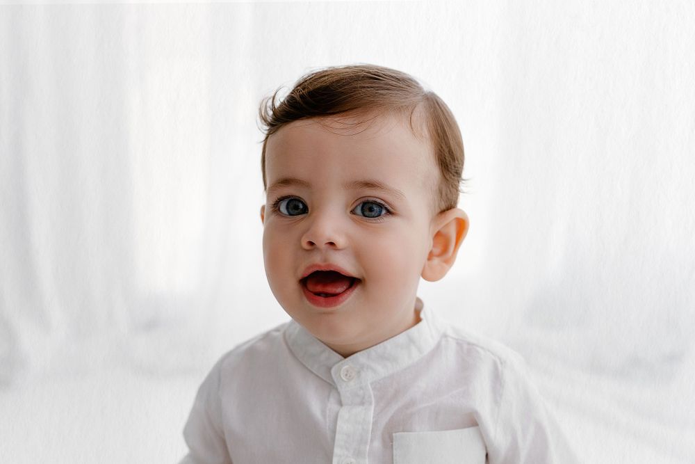 Baby wearing white button-up shirt smiles against light background.