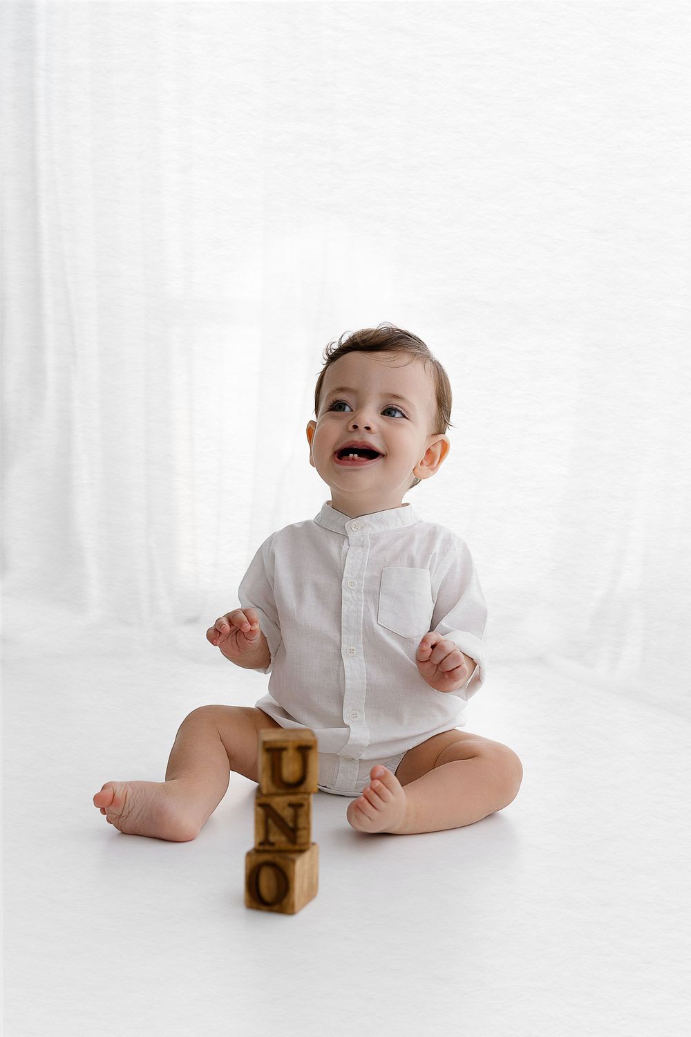 Baby in white shirt sits with wooden alphabet blocks on floor.