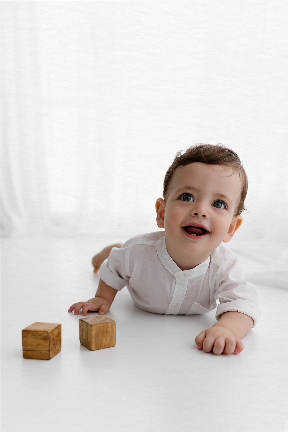 Baby in white shirt plays with wooden blocks on white surface.