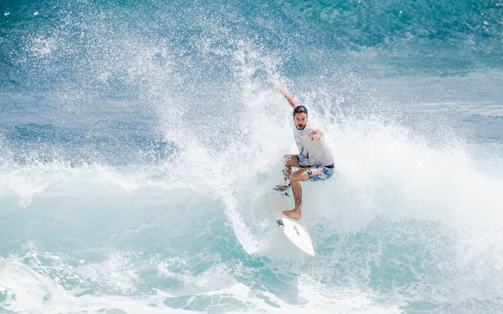Surfer executes an aerial maneuver on a turquoise wave with white spray flying.