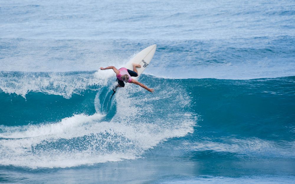 Surfer executes dramatic turn on turquoise wave creating dynamic spray pattern.