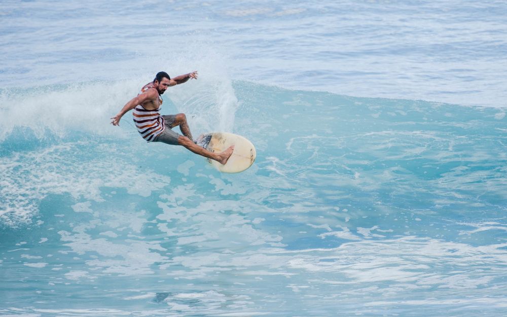Surfer rides wave in striped shirt performing stylish maneuver on yellow surfboard.
