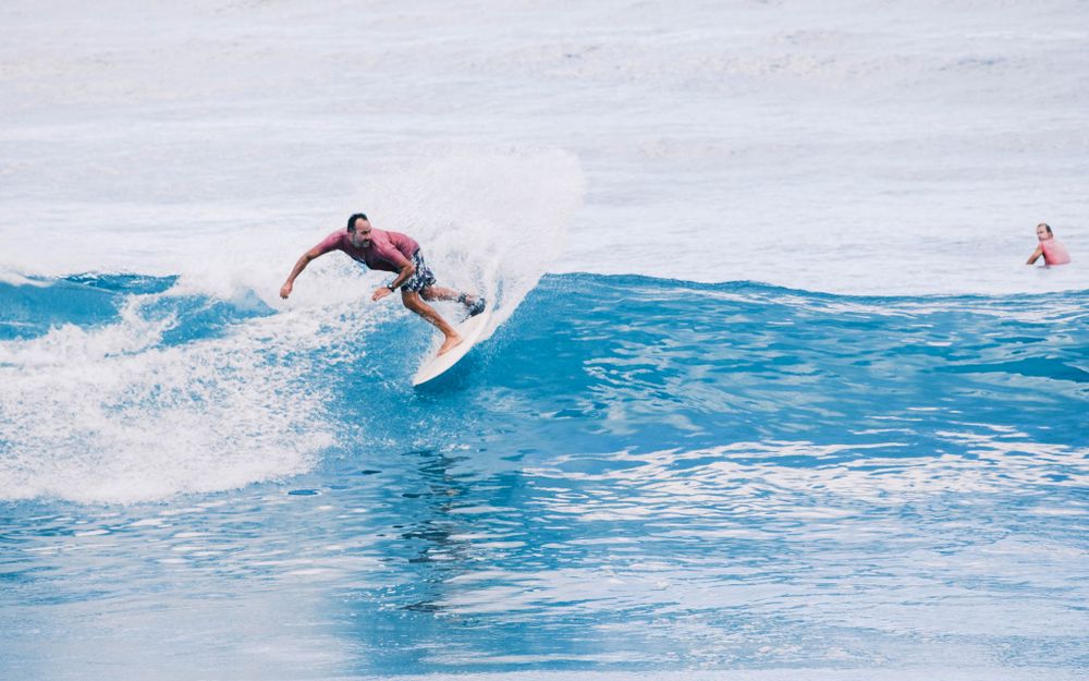 Two surfers catch waves in crystal blue ocean water with dramatic white spray.