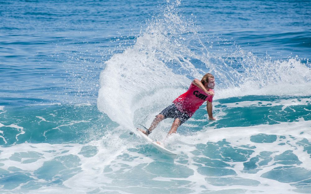 Surfer in red shorts performs powerful turn creating explosive splash on ocean wave.
