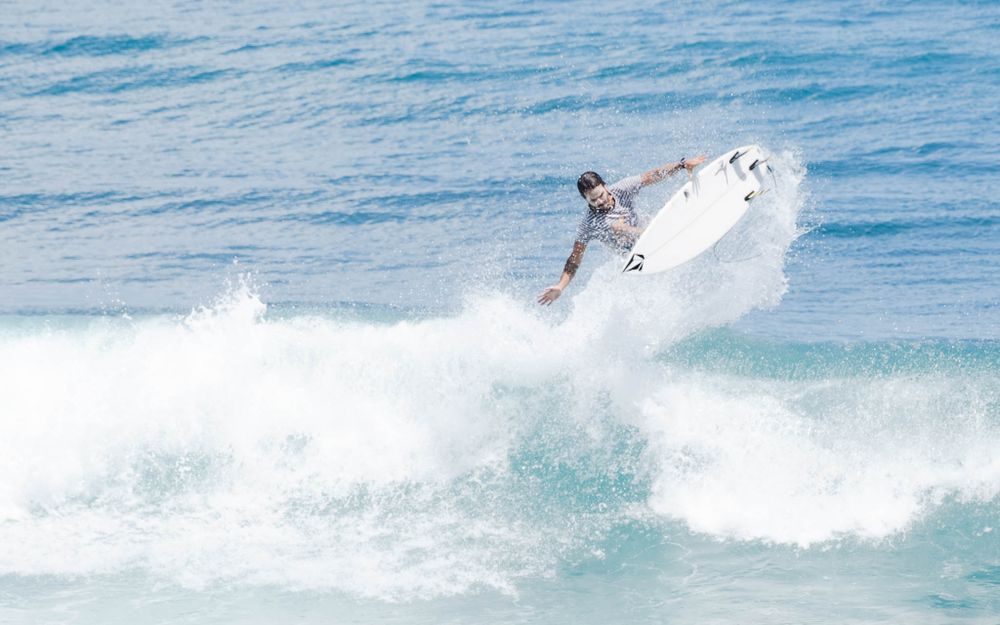 Surfer launches high into the air performing aerial maneuver above white ocean spray.