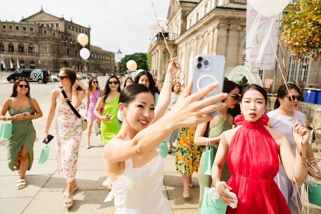 Joyful wedding guests celebrate on cobblestone street with historic architecture in background.
