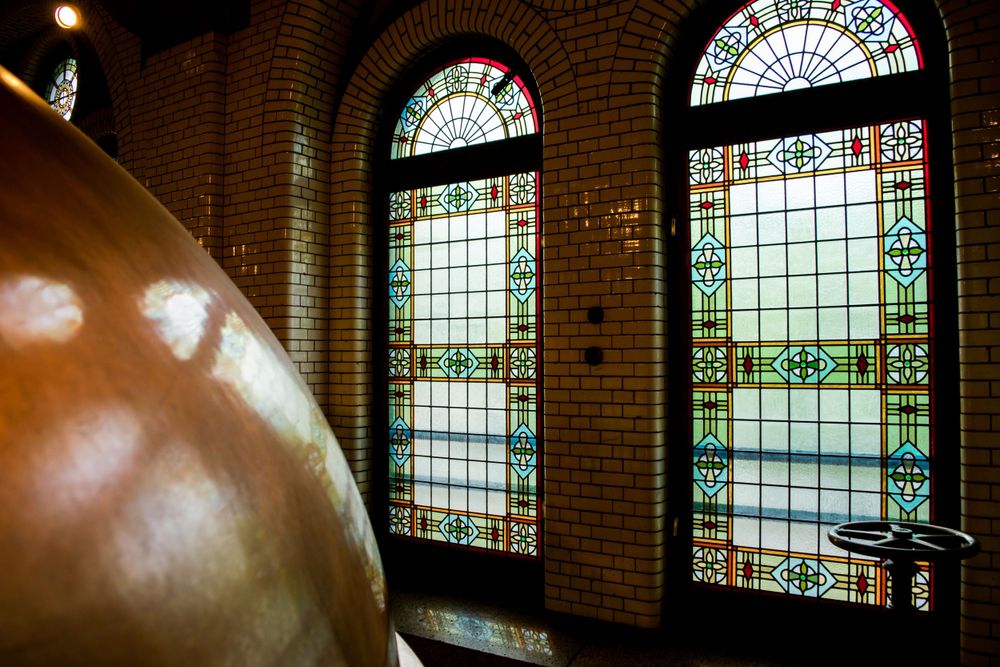 Stained glass windows and copper brewing tank in historic brewery building.