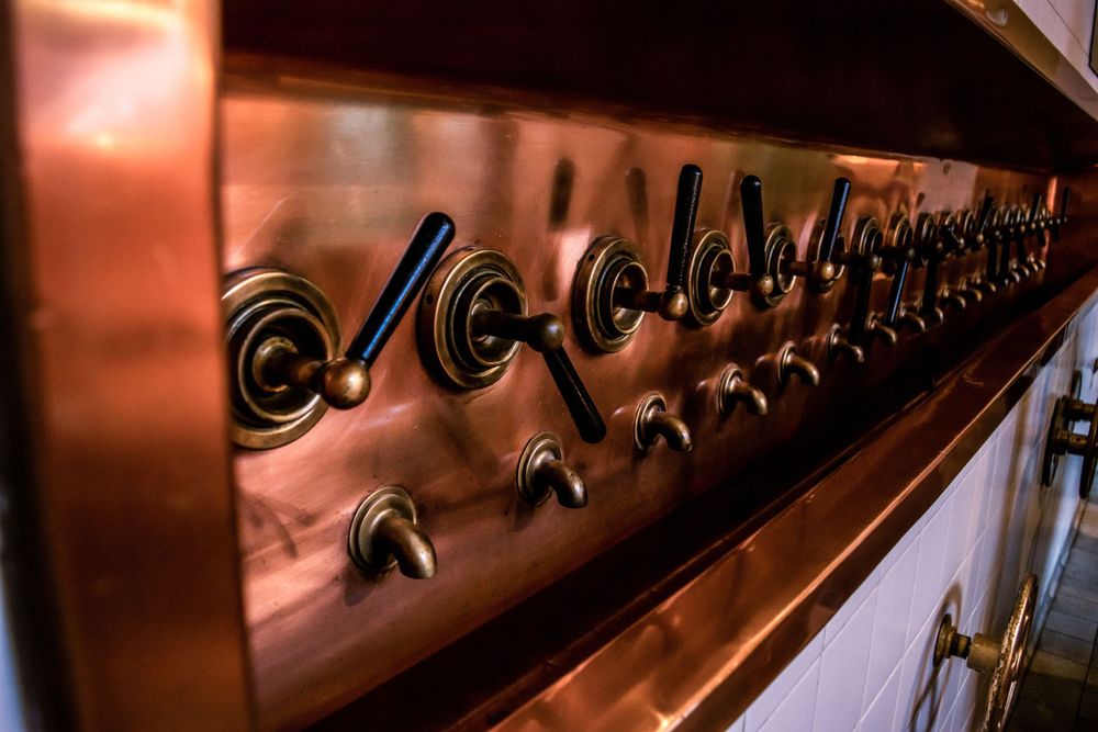 Row of copper beer taps lined up on bar counter with dramatic lighting.