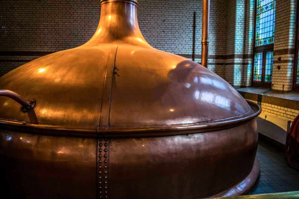 Large copper brewing kettle or distilling vessel with riveted construction in dim lighting.