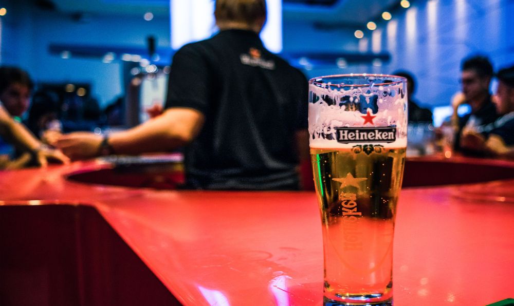 Glass of beer on red bar counter with blurred background in pub setting.