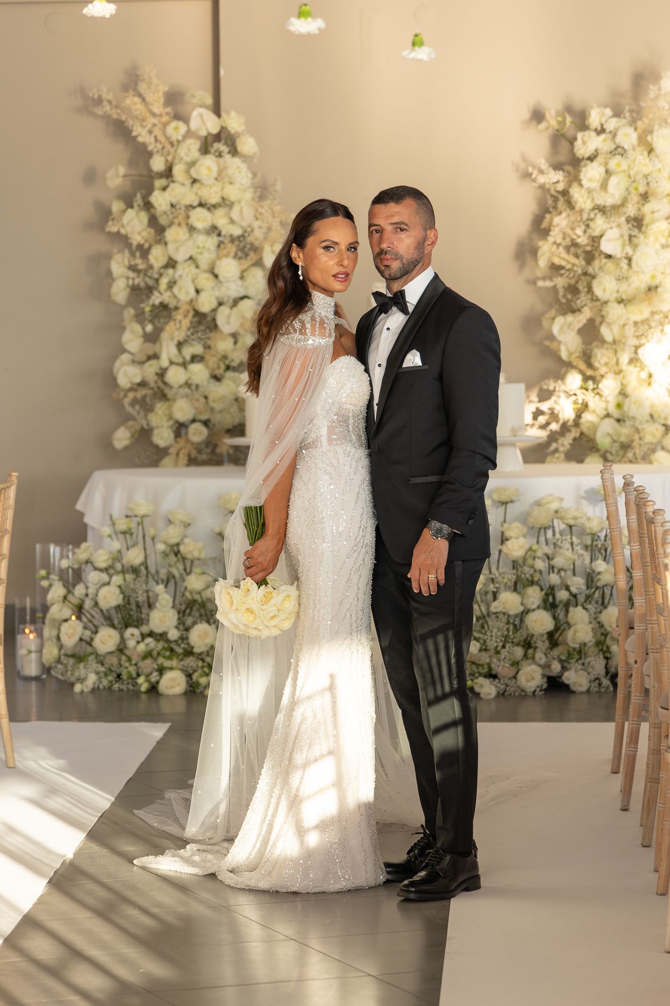 Wedding couple posing in modern venue decorated with white floral arrangements.