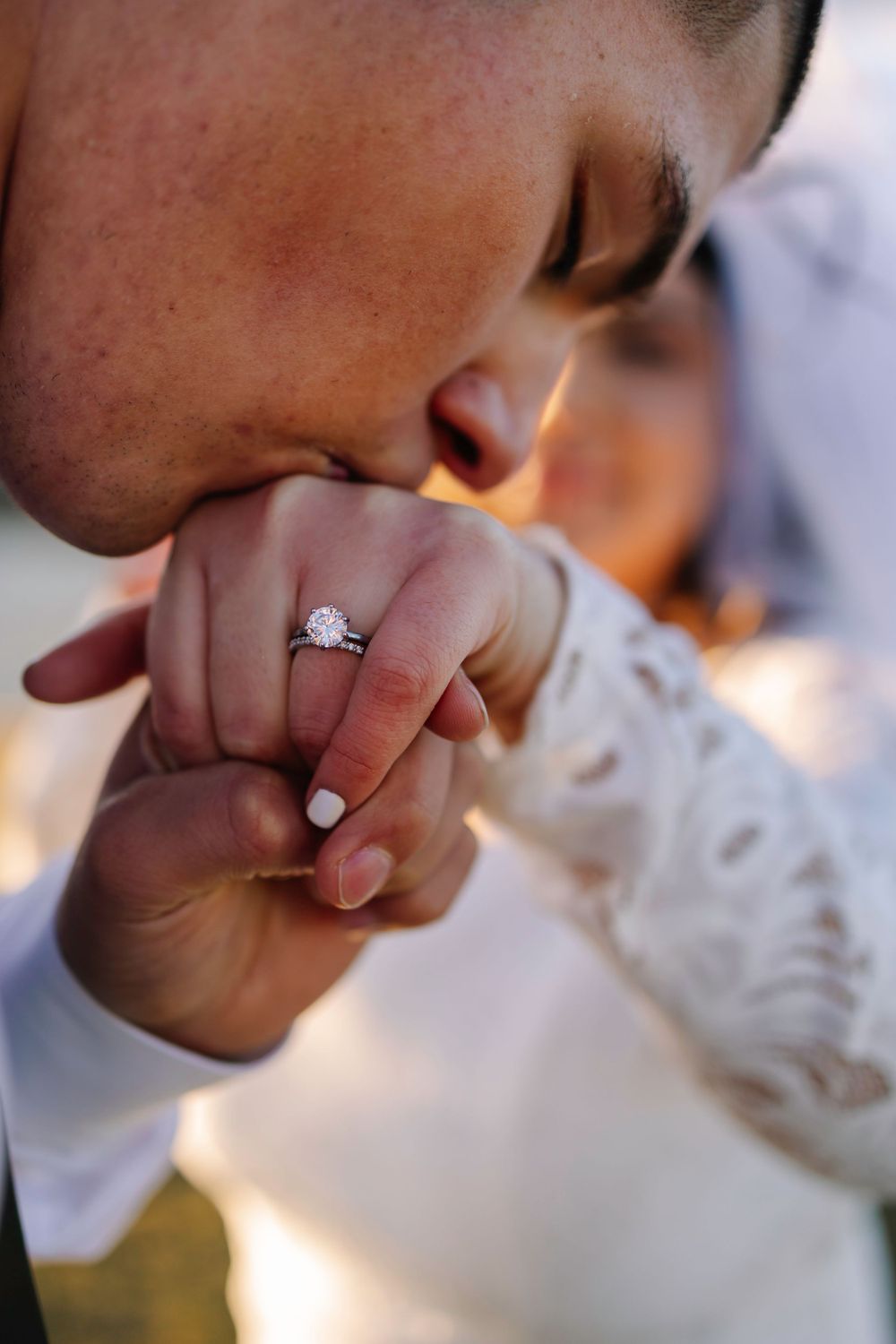 Romantic close-up of gentle kiss on hand showing engagement ring with sunlit backdrop.