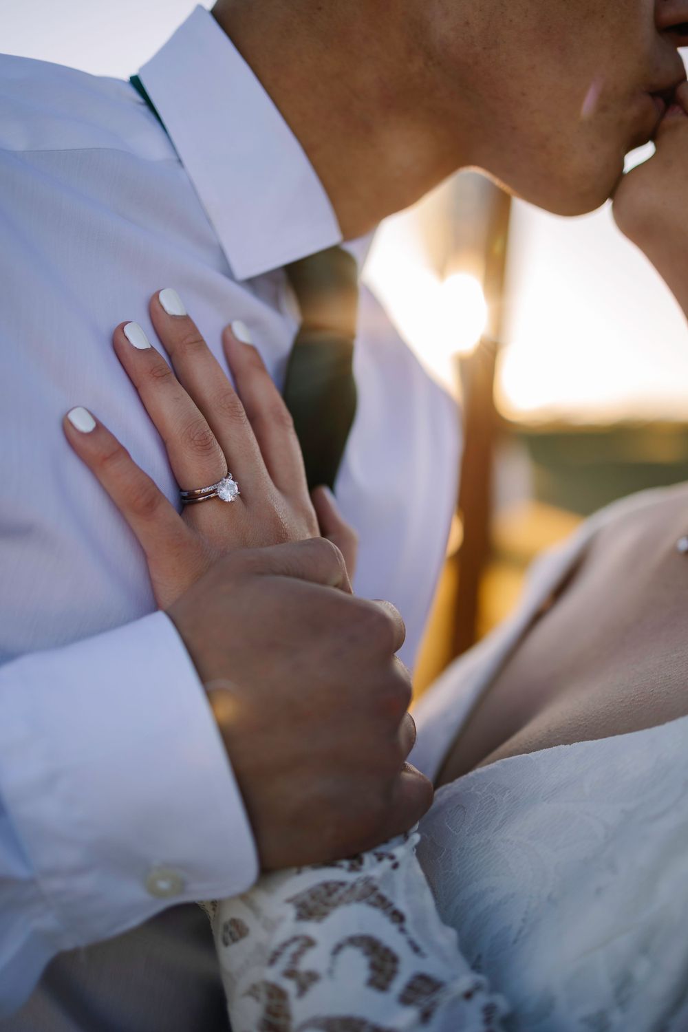 Close-up of wedding ring on hand against white dress and formal attire in warm sunlight.