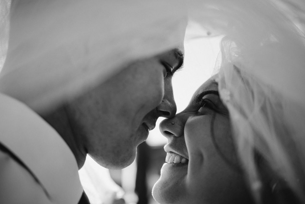 Close-up black and white intimate wedding portrait of couple under veil sharing romantic moment.