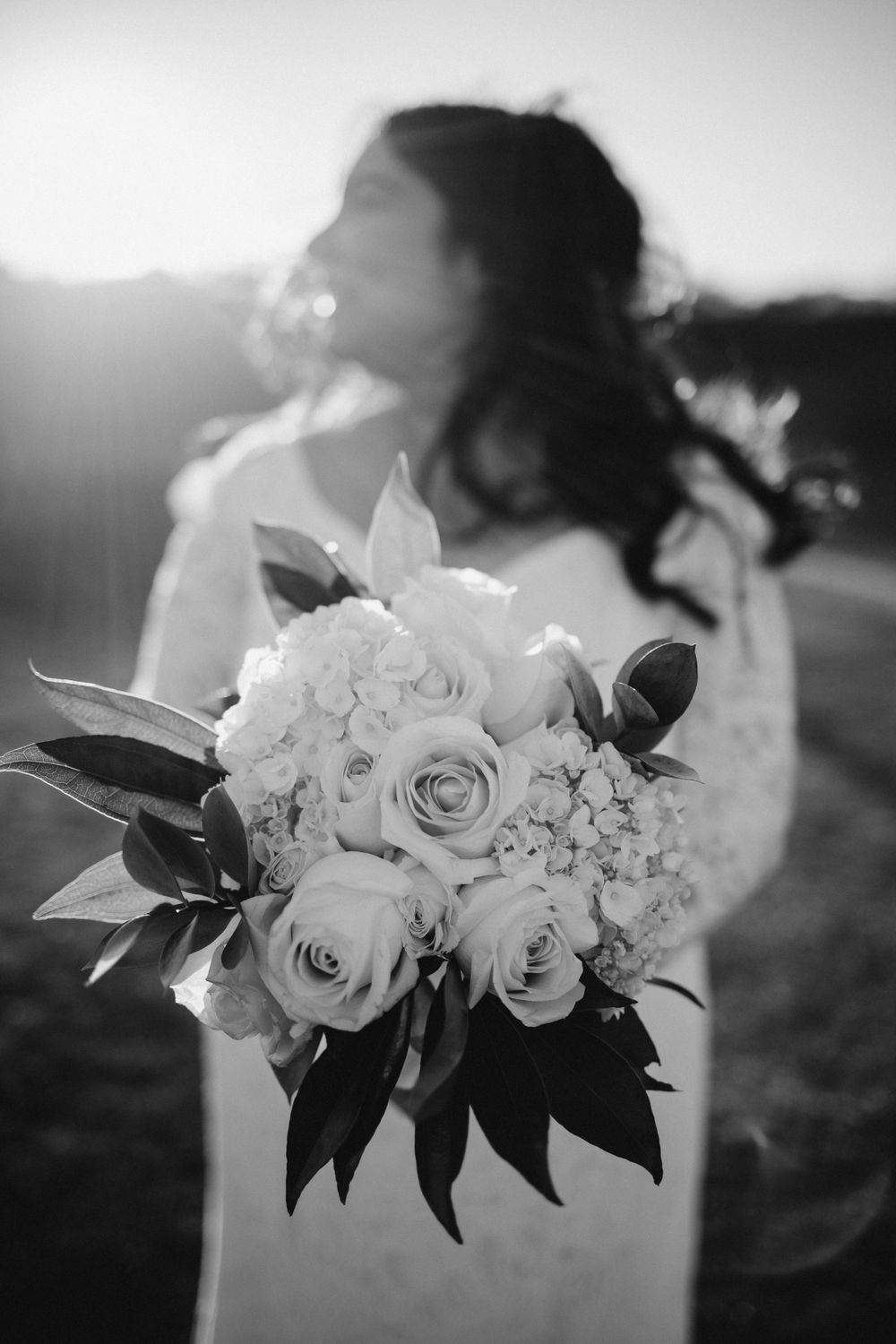 Black and white photo of bridal bouquet with roses and hydrangeas against sunset.