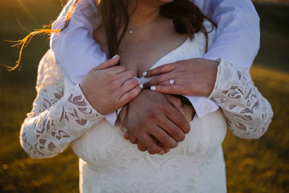 Close-up shot of embracing hands with lace sleeve details in golden sunlight.
