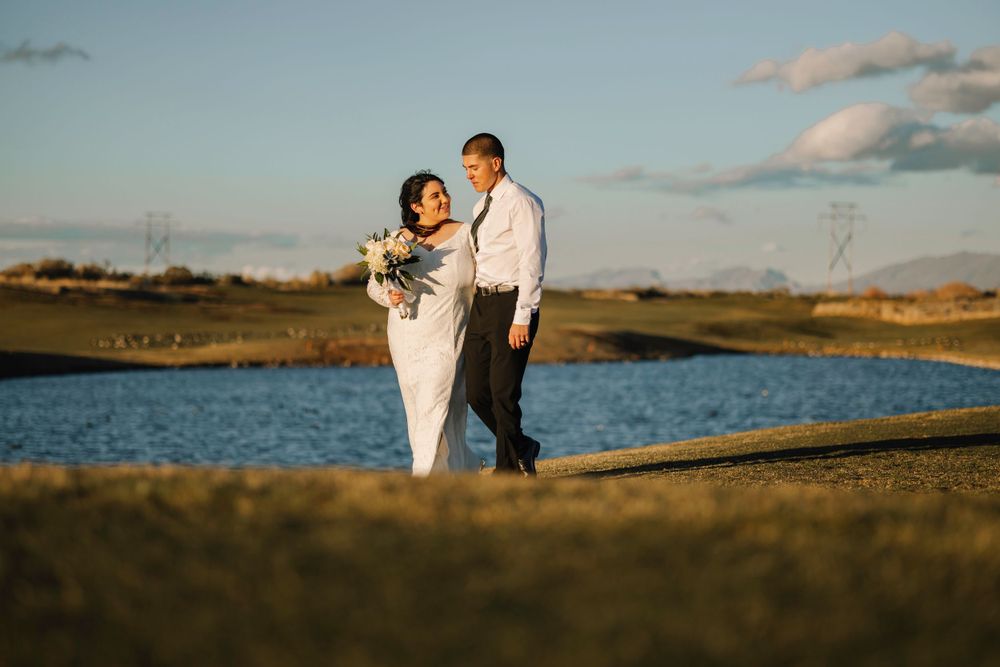 Wedding couple standing by waterfront during golden hour sunset.