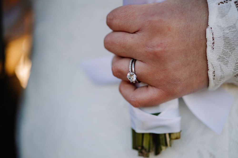 Close-up of engagement ring on hand holding wedding bouquet.