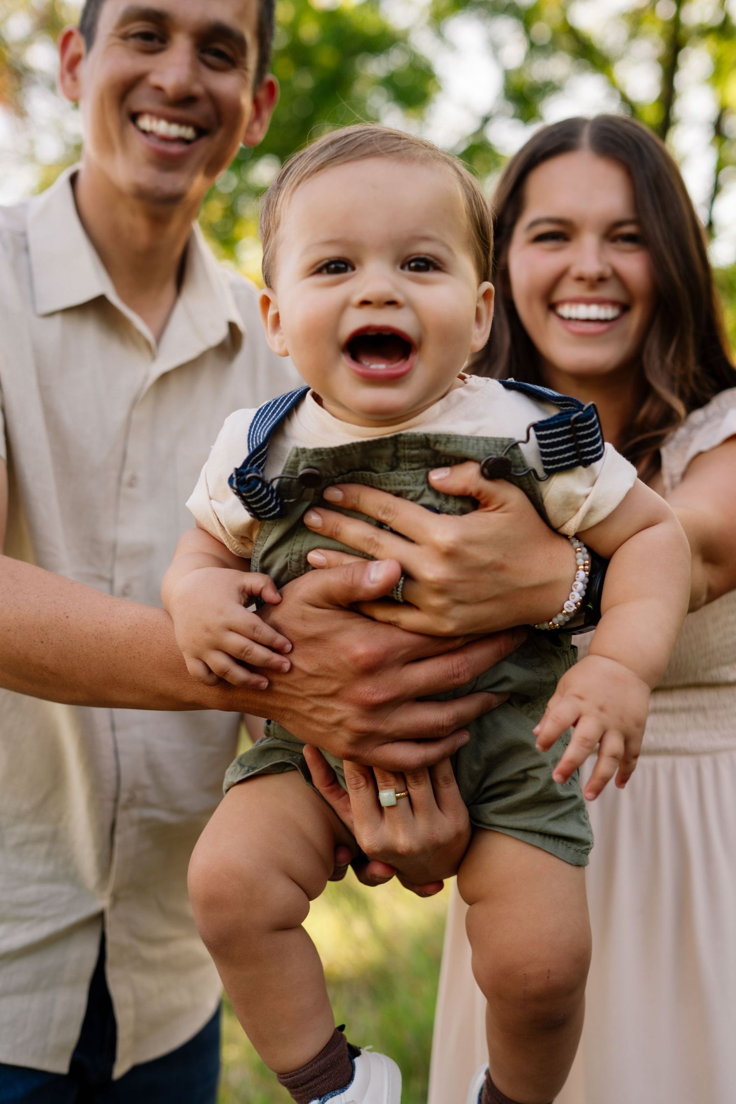 Baby in camouflage outfit laughs during outdoor family photo session.