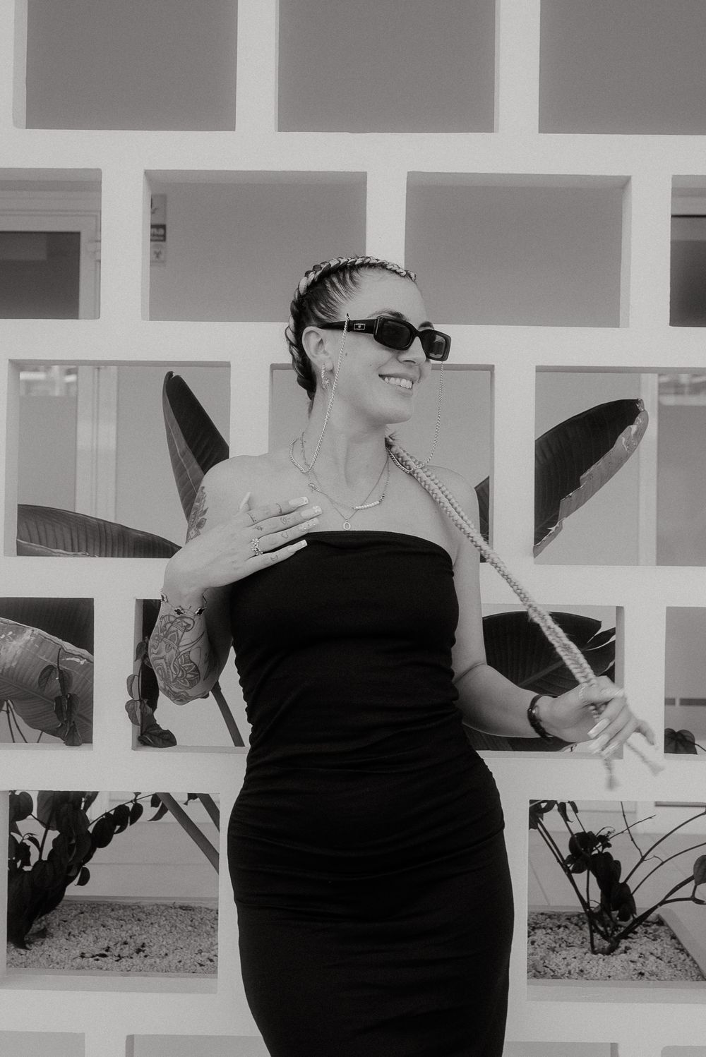 Person in black dress with cornrow braids poses against geometric white wall.