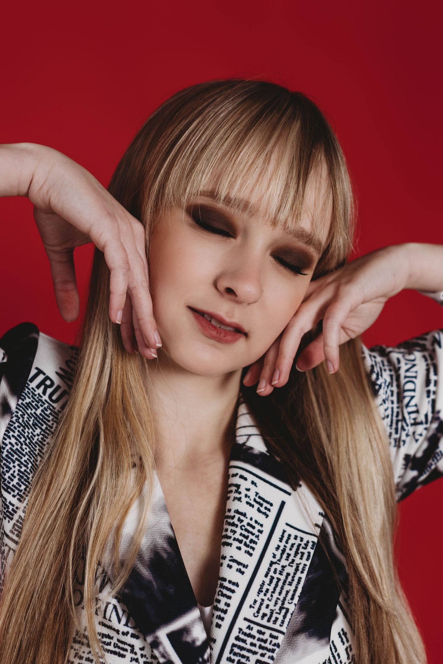 Fashion model wearing black and white newsprint pattern outfit poses against red background in artistic portrait series.
