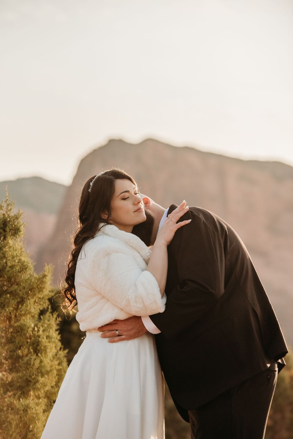 A romantic couple embraces during their wedding photoshoot against a beautiful desert mountain backdrop at golden hour.