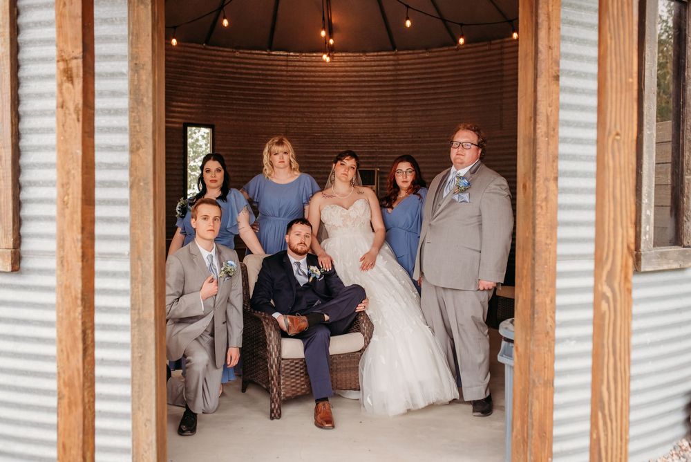 Wedding party poses together in rustic wooden gazebo with string lights overhead.