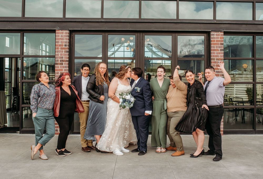 Wedding party poses together in front of modern brick and glass building entrance on sunny day.