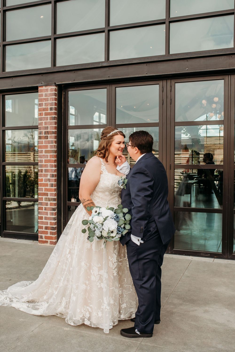 Newlywed couple shares an intimate moment outside a modern brick building with large windows.