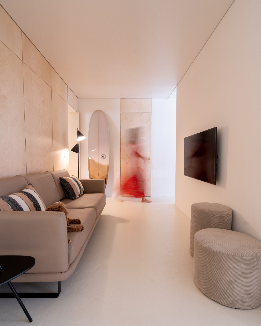 Modern minimalist living room with white walls, grey sofa, and blurred motion figure in red.