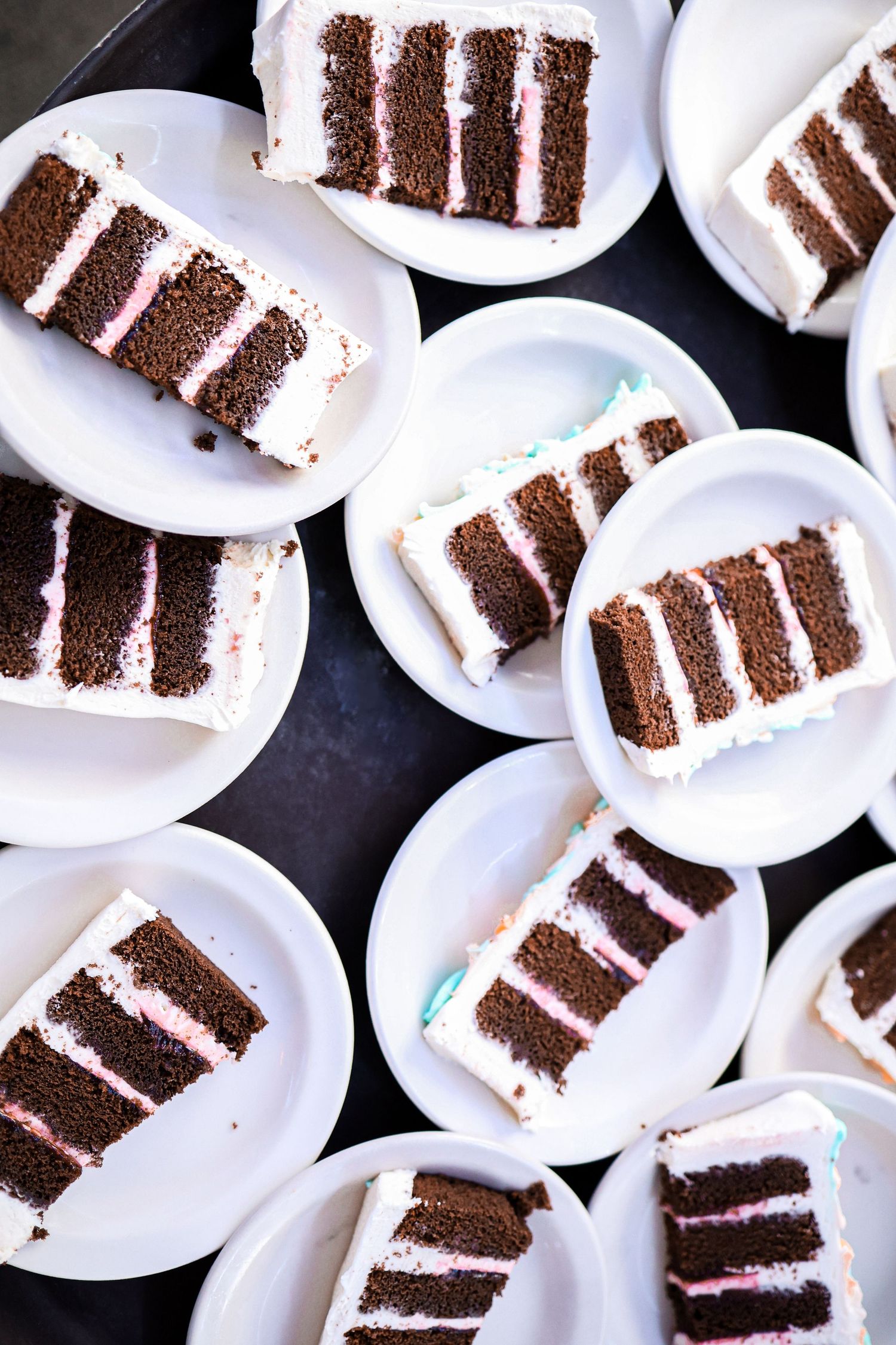 Multiple plates of layered chocolate wedding cake with white frosting arranged on white dishes.