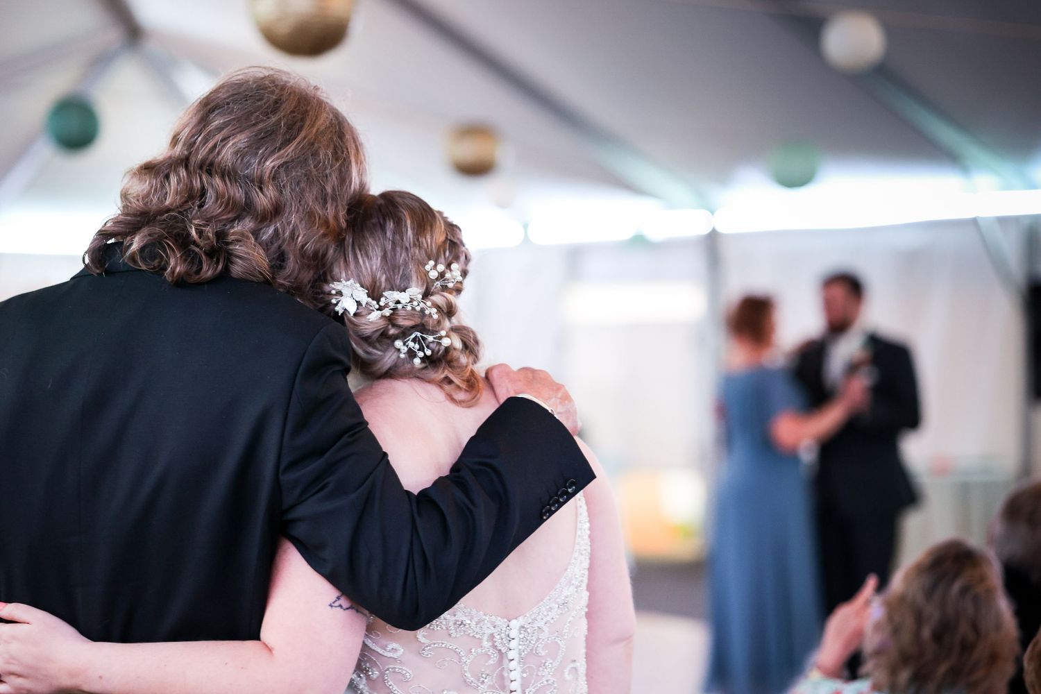 Intimate wedding dance moment under a tent with string lights and other couples in background.