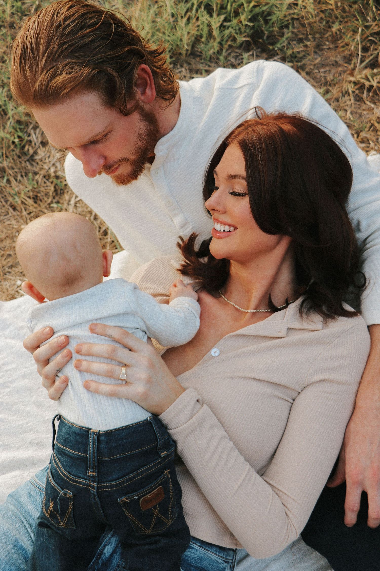 A family shares a joyful moment outdoors while holding their baby in a light blue outfit.