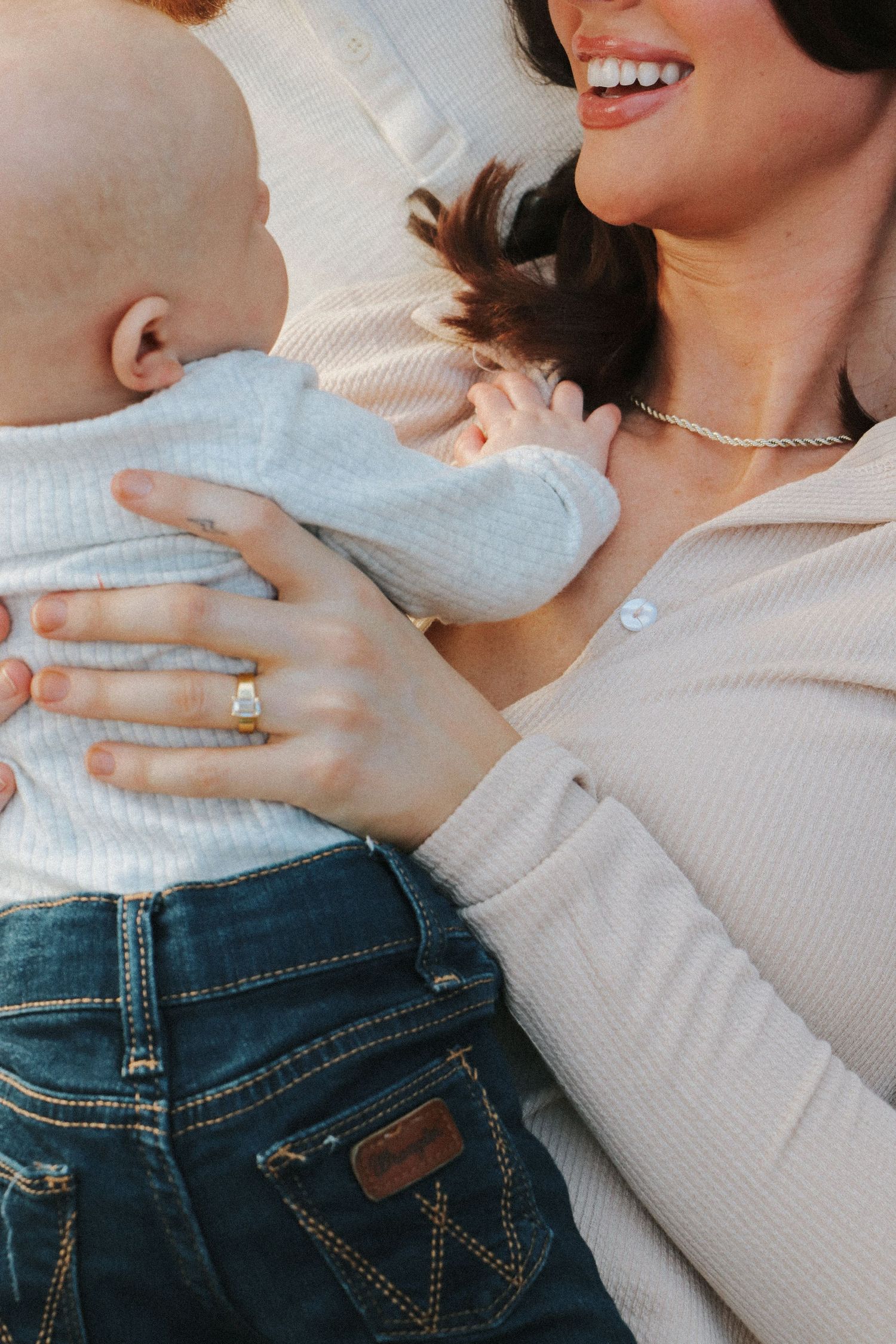 Close-up of a baby in light blue clothing being held, showing a ring on the hand holding them.