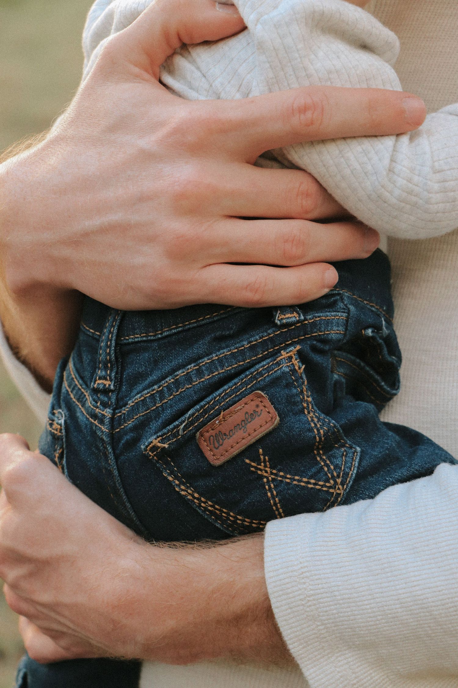 Close-up detail of hands holding a baby wearing Wrangler jeans.