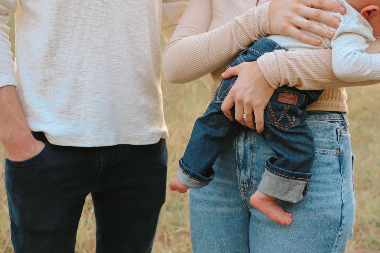 Cropped view of parents holding their baby, showing casual denim and white clothing.