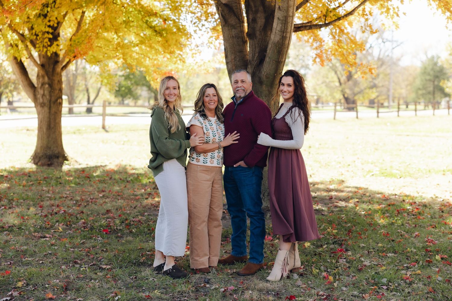 A group stands together outdoors under golden autumn trees in coordinating fall-toned outfits.