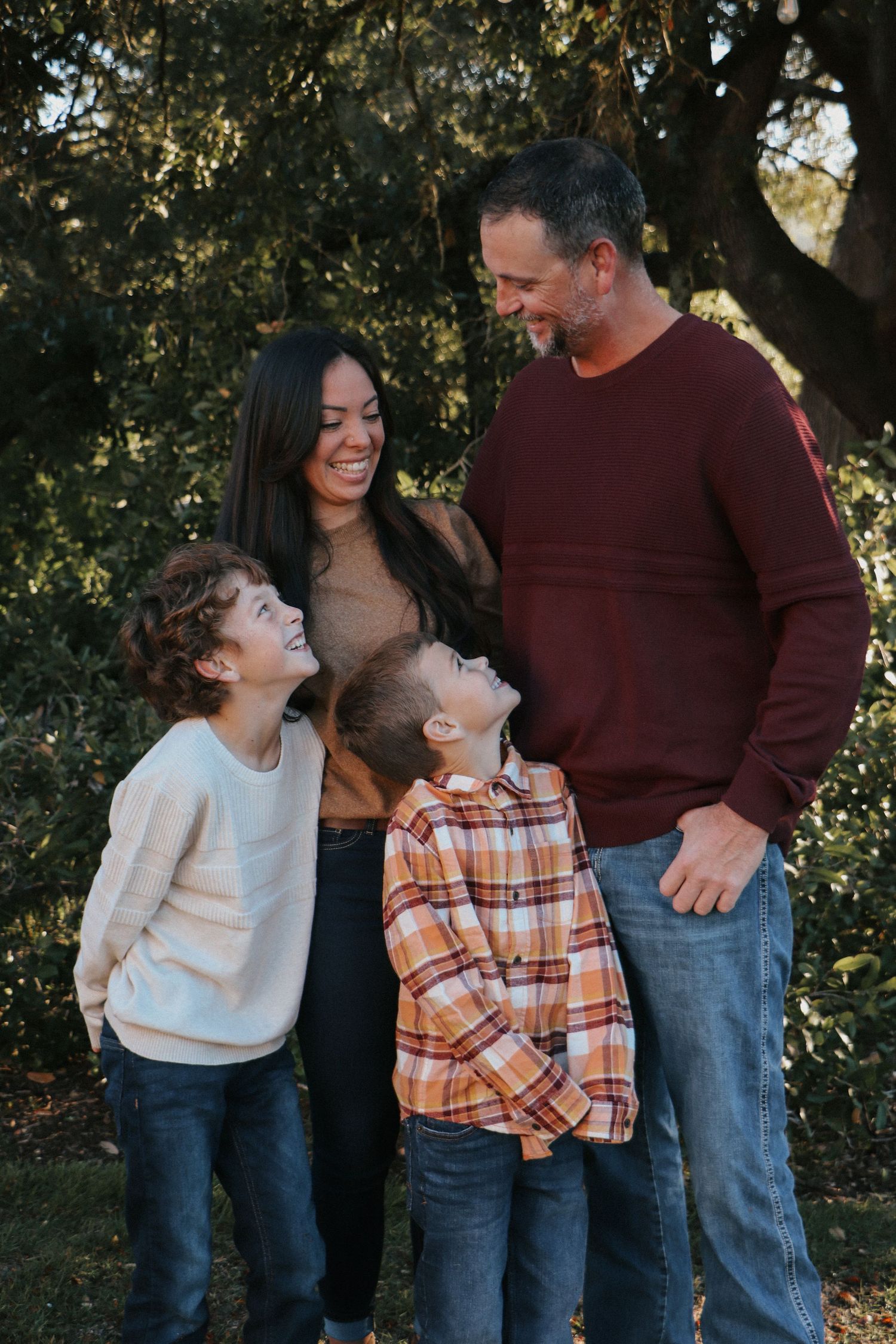 A family of four stands together outdoors against a backdrop of trees.