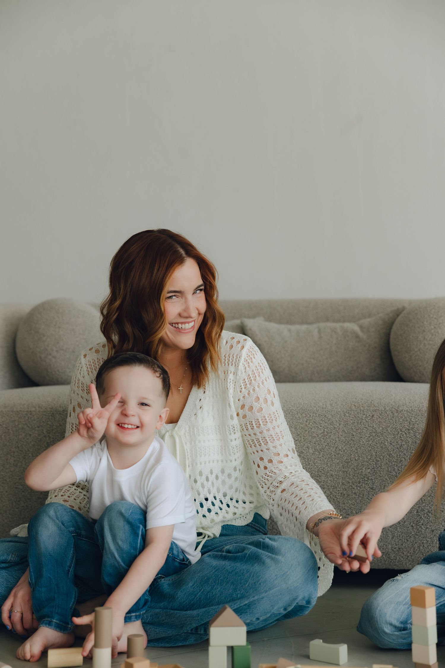 Candid moment of mother and child playing with wooden blocks while sitting on a gray couch.