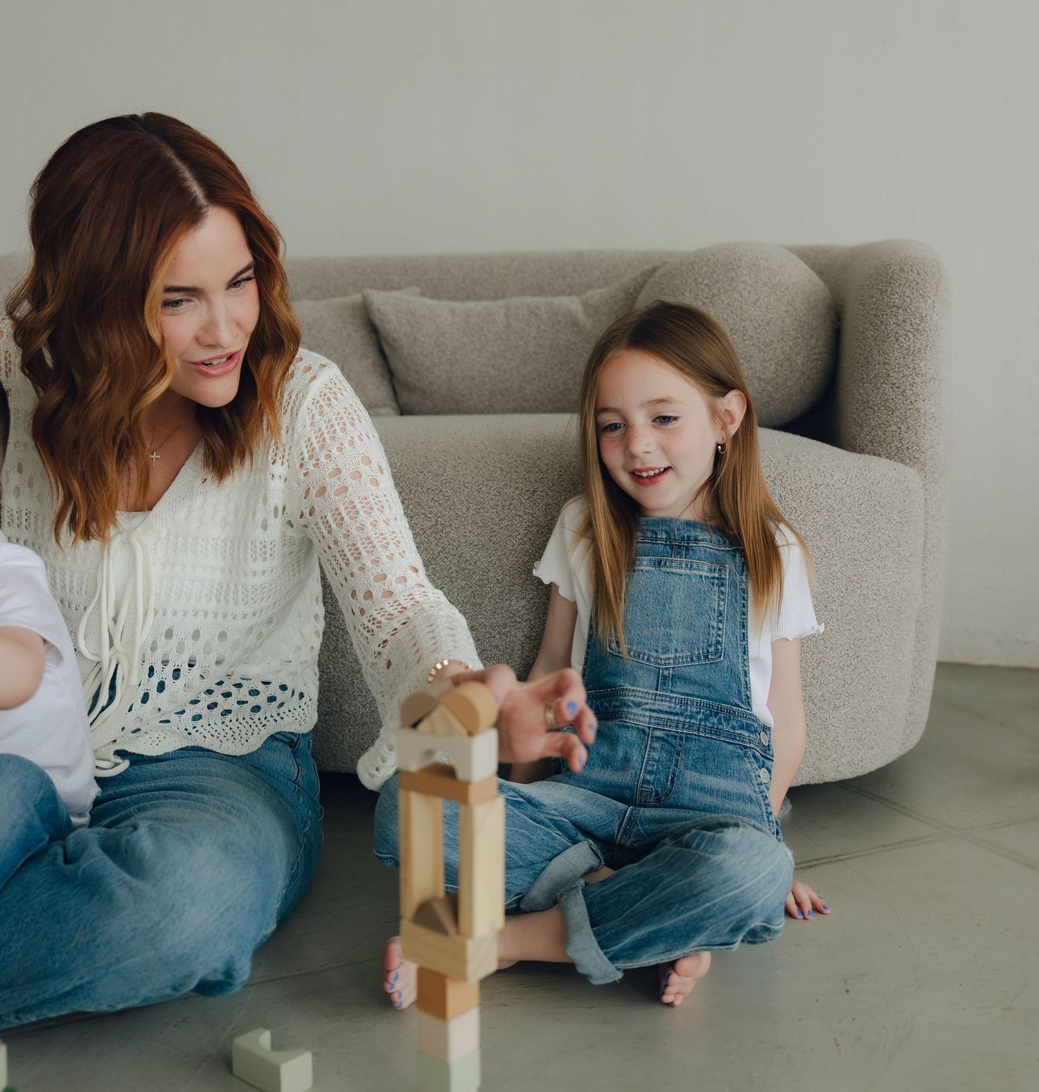 Two people sit on floor at home and play together with wooden stacking blocks while sharing joyful expressions.