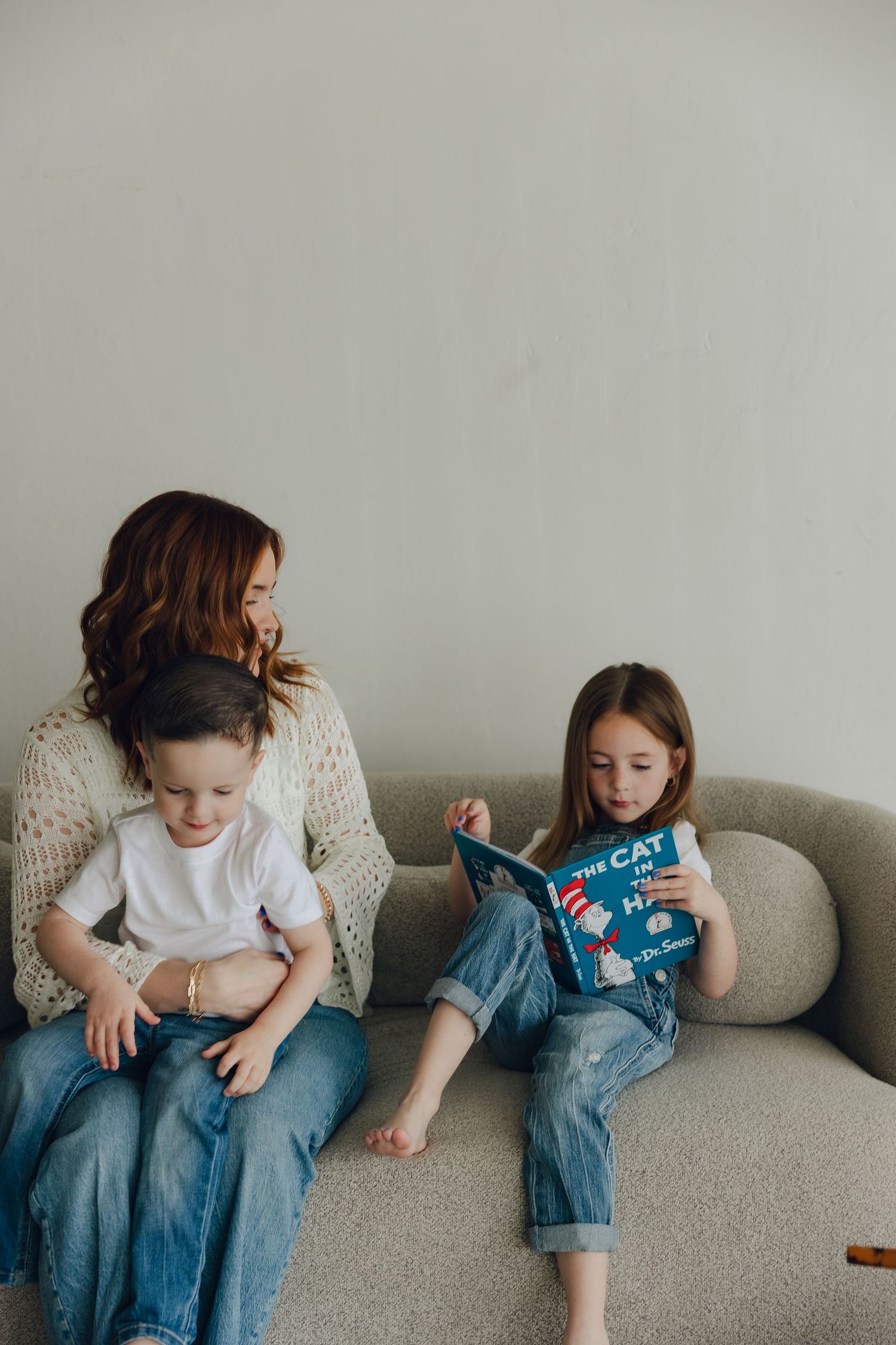 Reading time on a comfy gray sofa as a child enjoys a book while the others look on.