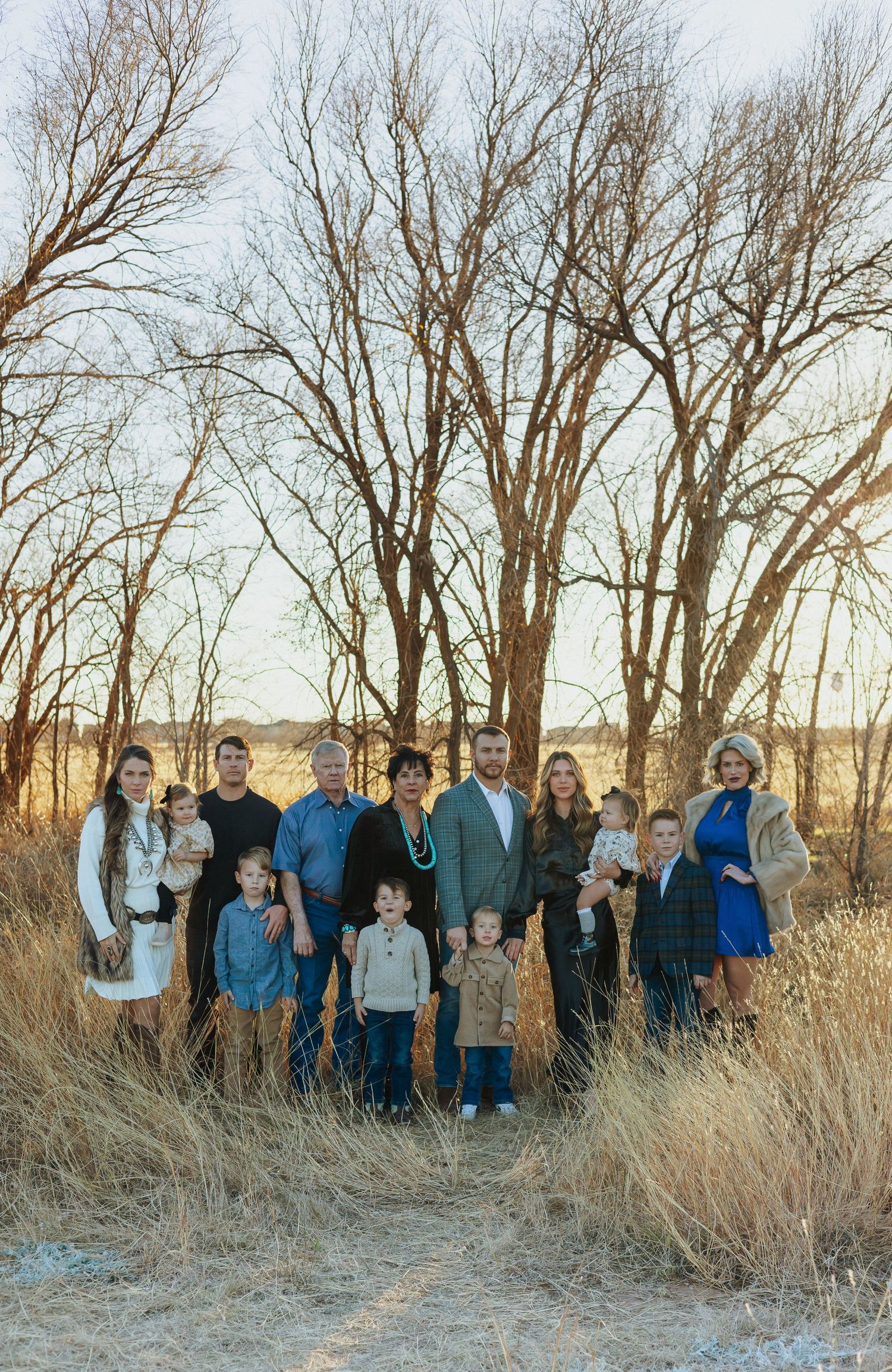Large group portrait in natural field setting with bare trees at sunset.
