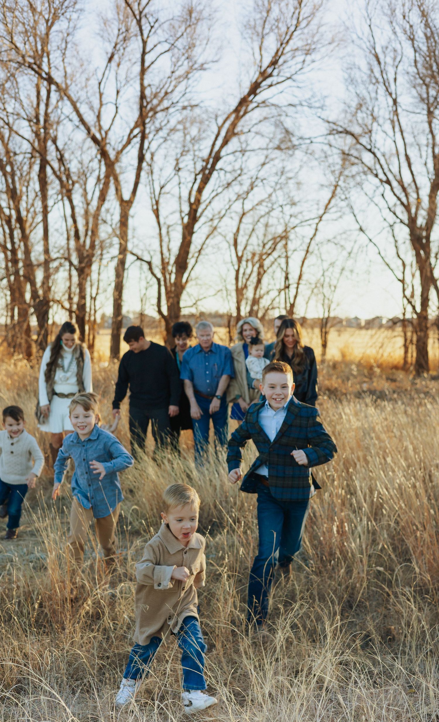 Group of people running playfully through tall grass at sunset.