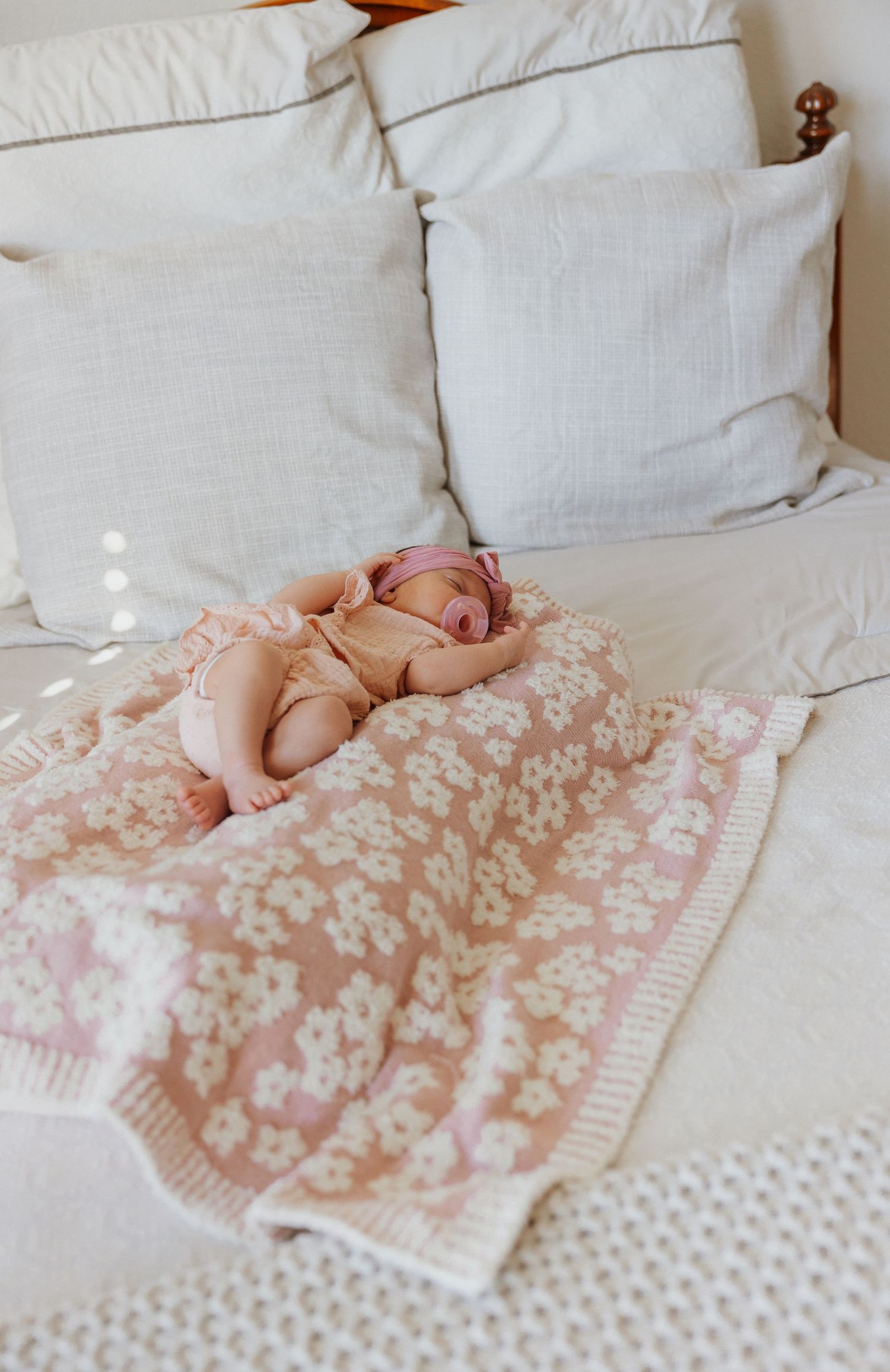 Sleeping baby on white couch with floral blanket and pillows.