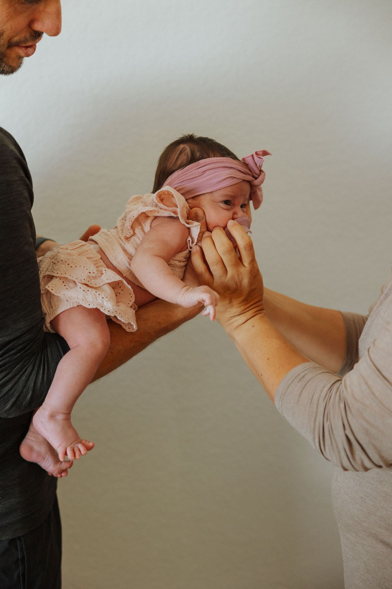 Parents playing peek-a-boo with baby in peach dress.