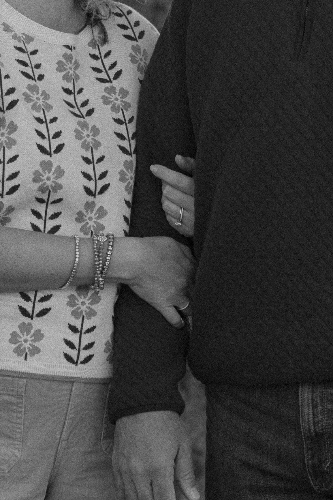 A black and white photo showing hands touching, with one person wearing a floral patterned top and bracelets.
