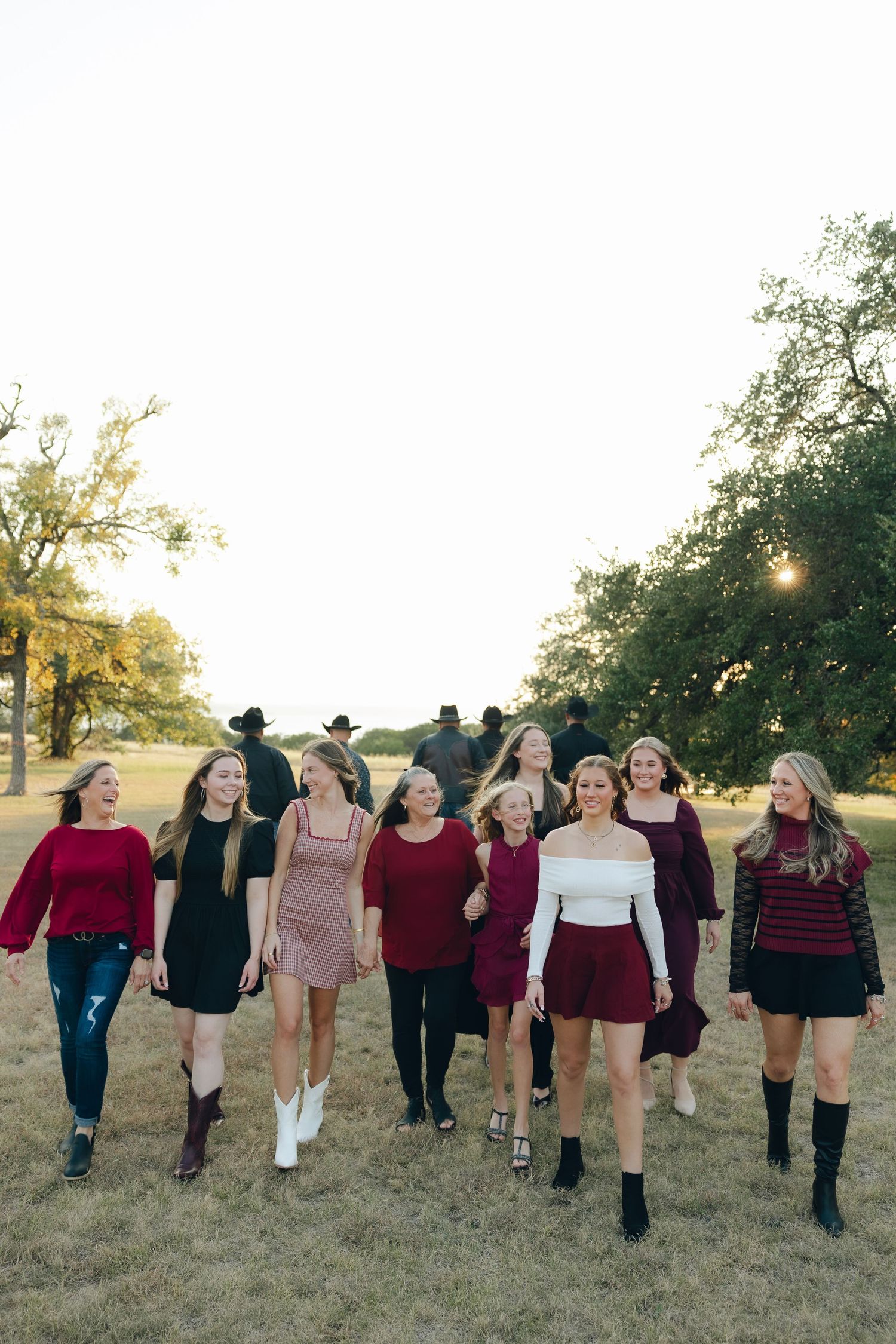 A group of friends in burgundy and black outfits walking together across a grassy field at sunset.