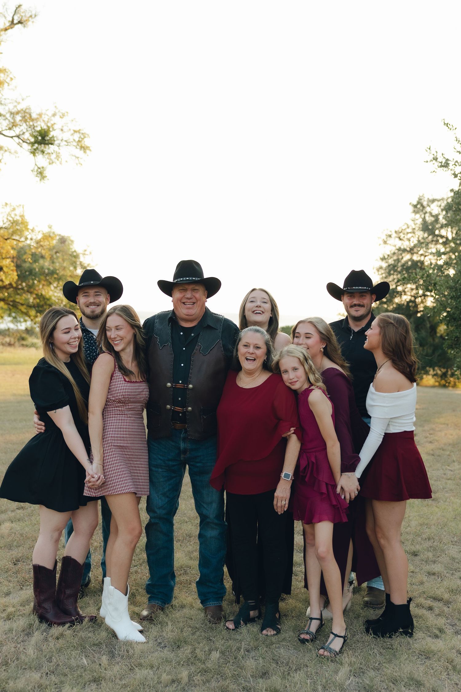 A group of people in western attire pose together outdoors during golden hour in a grassy field.