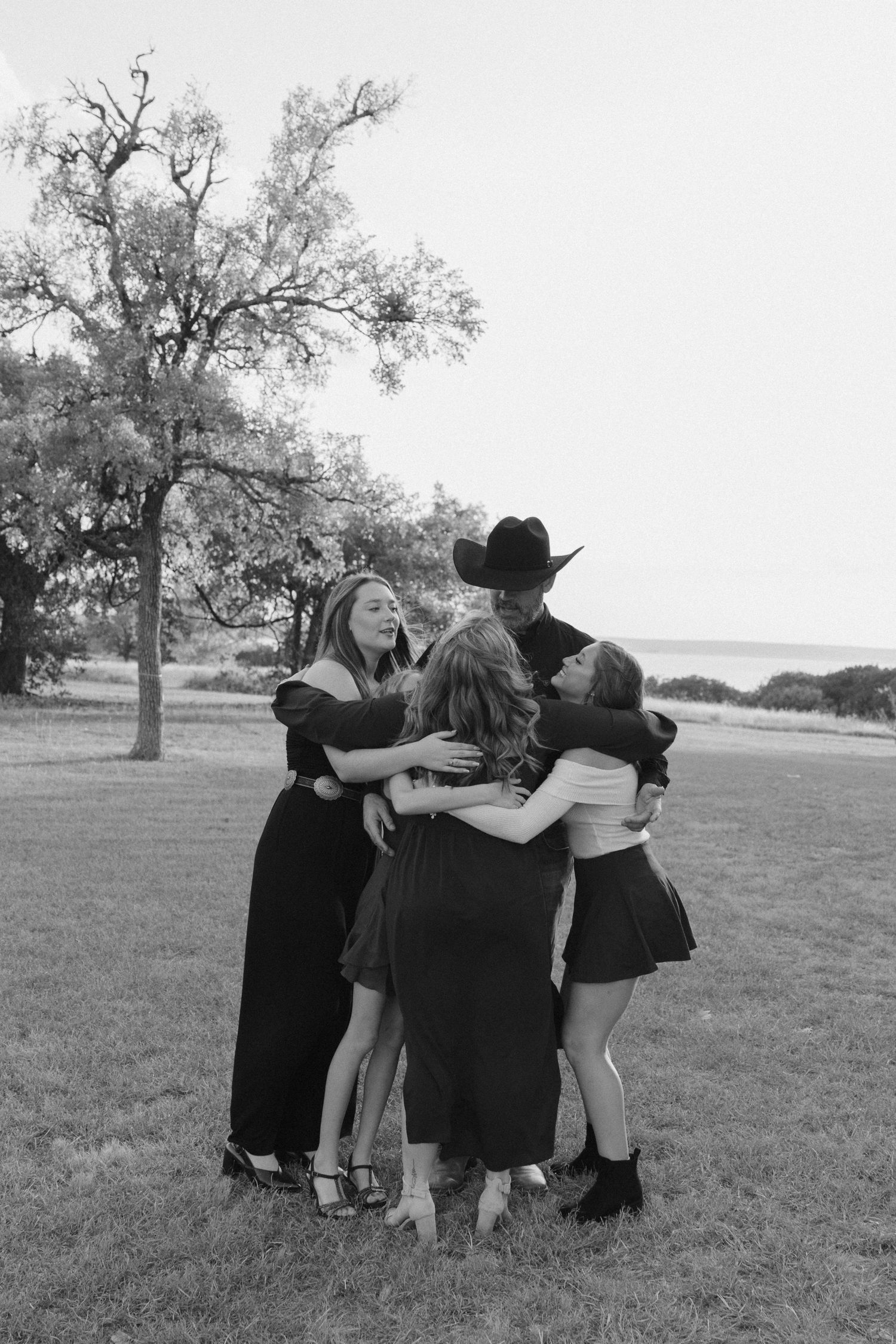 A group of friends huddle together in an outdoor field, sharing a joyful moment in black and white photography.
